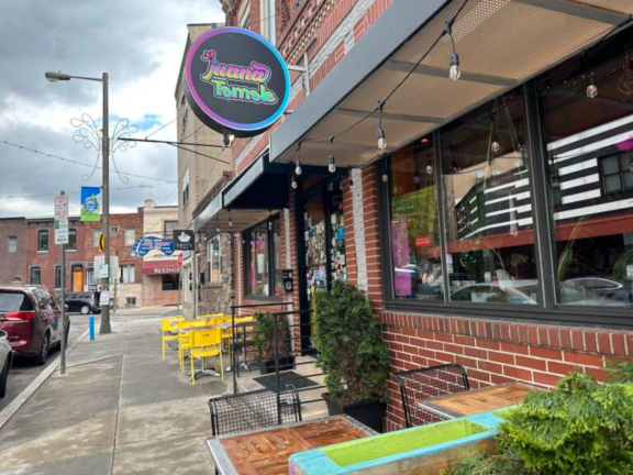 Facade of Juana Tamale restaurant including outdoor tables and sign