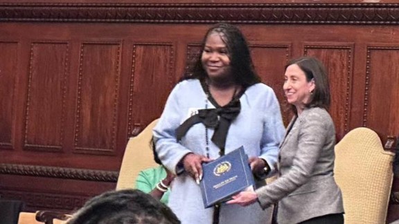 Tatyana Woodard being handed a blue binder by Councilmember Rue Landau during a ceremony that honors her participation on the Philadelphia Commission for Women.