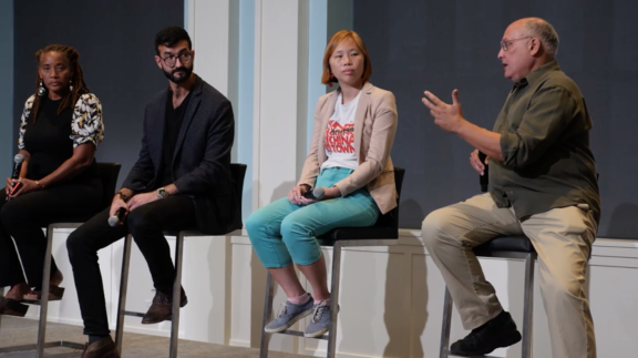 Four panelists sitting in stools on a stage