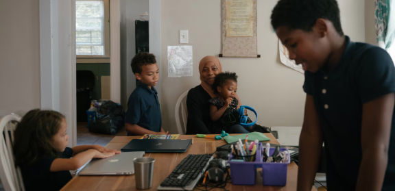 Sameerah Abdullah holds her daughter Maimoonah Abdul Hakeem, 3, while her children Asiyah Jones (left), 6, Dawud Jones, 7, and Musa Moore, 9, do schoolwork in their home in Philadelphia