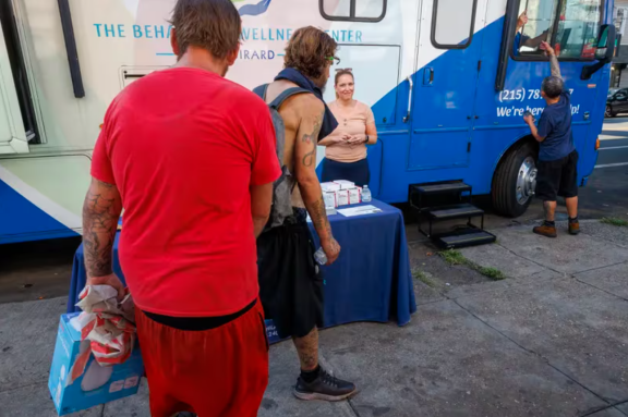 People along Kensington Avenue walk past the mobile home belonging to the Behavioral Wellness Center at Girard