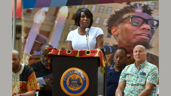 Celena Morrison-McLean speaking in front of a podium during a street dedication for Michael Hinson, Jr.