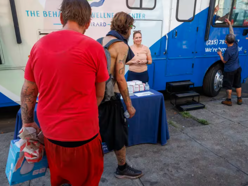 People along Kensington Avenue walk past the mobile home belonging to the Behavioral Wellness Center at Girard