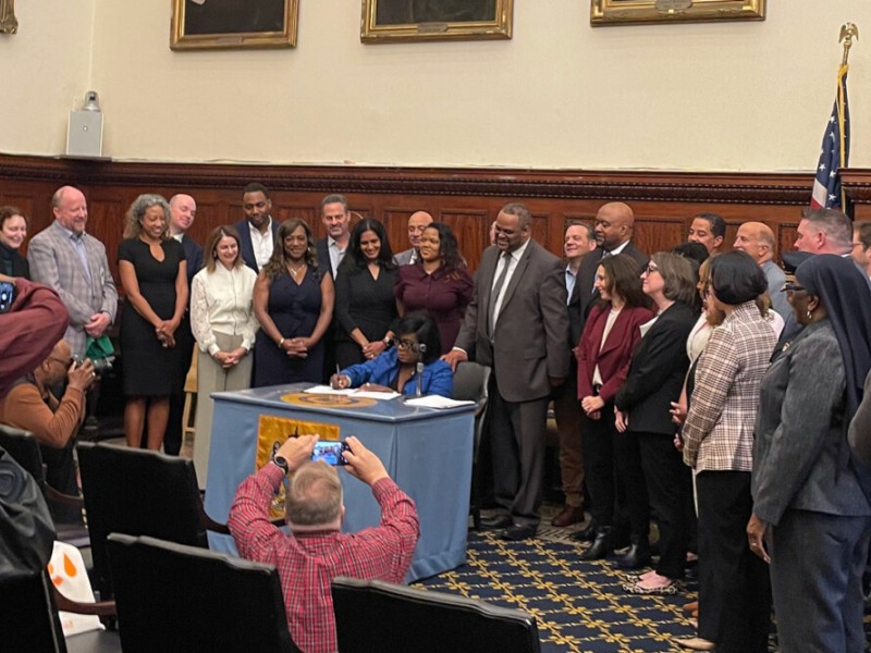 Mayor Cherelle Parker signing a paper with city officials standing around her